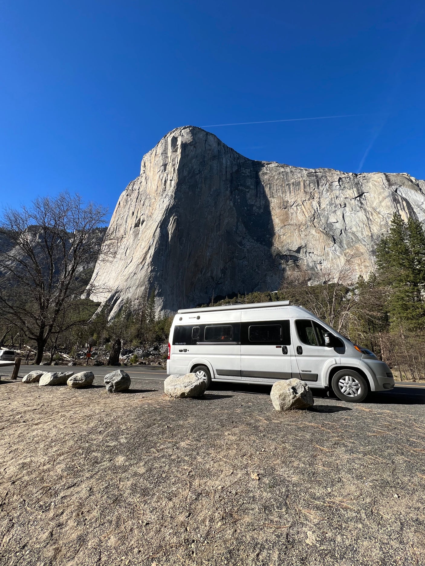 An rv rental camper van rests before Yosemite's El Capitan, a towering granite cliff under a clear sky. A perfect scenic travel spot!