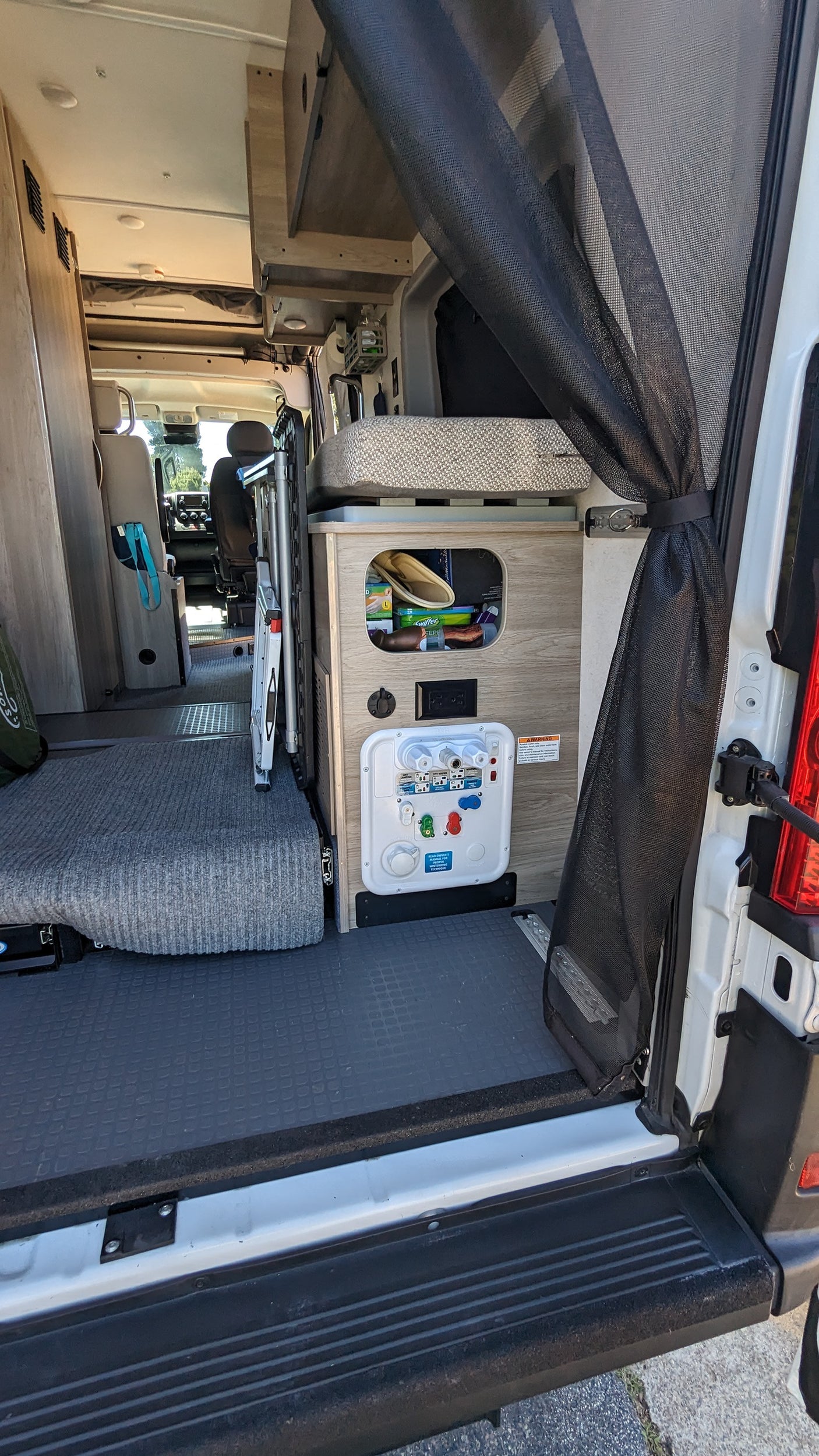 RV rental interior: open rear door reveals a versatile living space with adaptable seating, storage, and utility panel.
