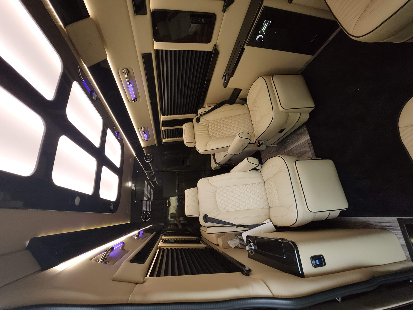 Inside this premium RV rental: A lavish custom van interior with cream quilted seats, sleek black accents & soft lighting.