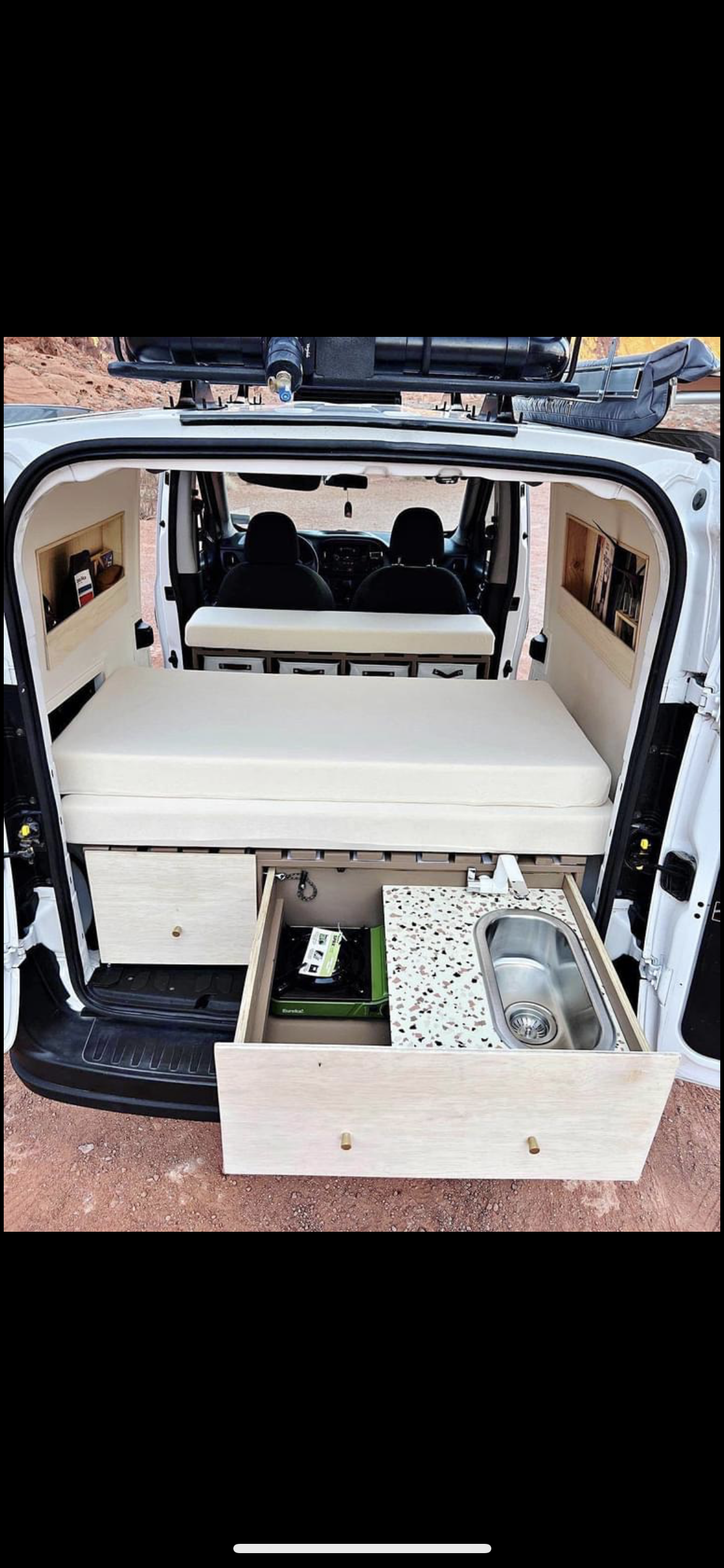 Compact RV rental: White camper van interior with a cozy bed, pull-out kitchen (stove & sink), and built-in storage.