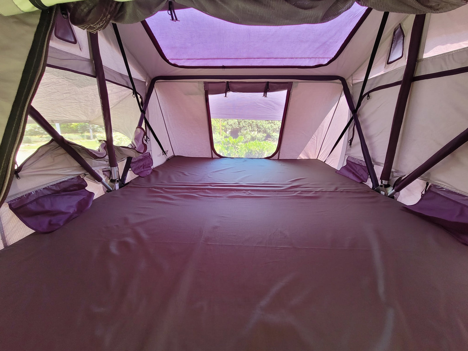 Interior of a cozy rooftop tent setup, featuring a dark mattress, mesh windows, and structural poles, perfect for RV rental adventures.