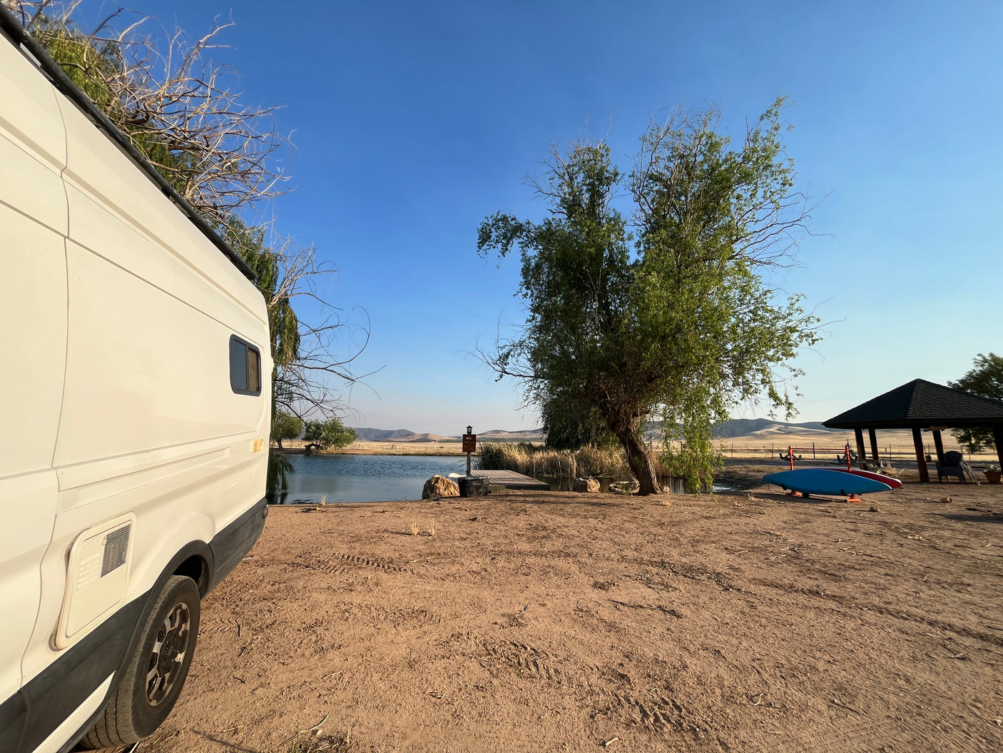 RV rental by a scenic lake, featuring a campervan, kayaks, and a gazebo. Ideal for nature and outdoor adventure.