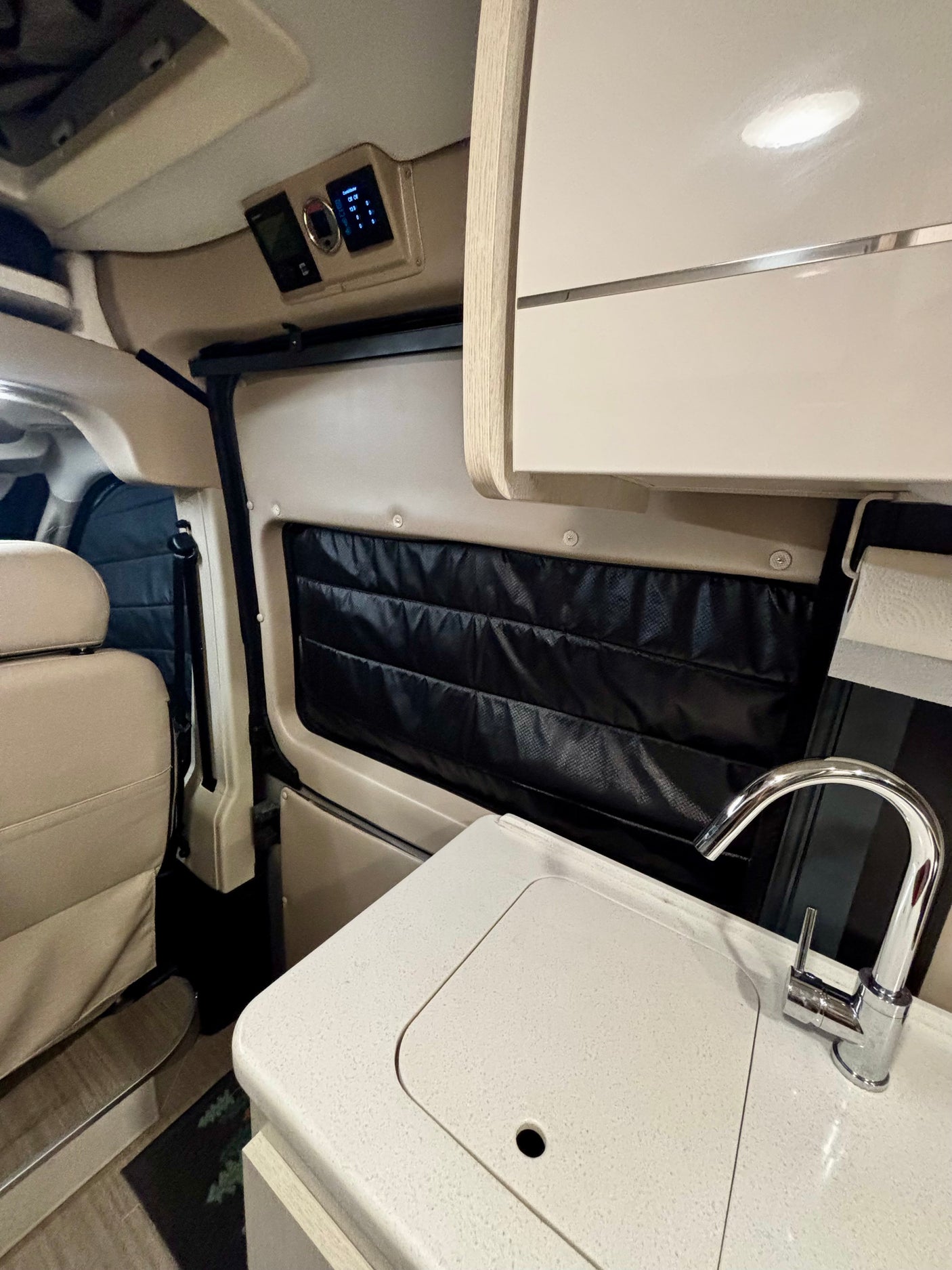 Modern RV rental interior featuring a kitchen sink, overhead cabinets, and climate controls, ideal for comfortable travel.