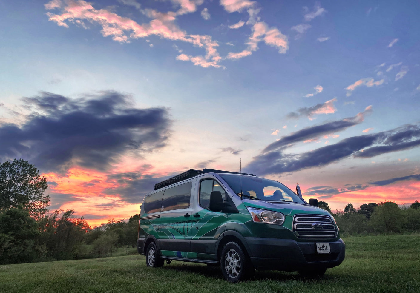 Vibrant sunset over a custom green RV rental van in a grassy field, ready for your next camper adventure.