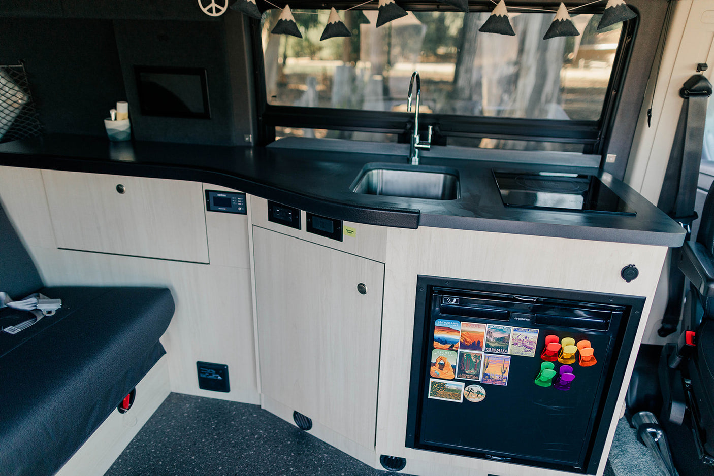 Inside an RV rental: a modern kitchenette with sink, cooktop, fridge, and ample light wood cabinetry for comfortable travels.