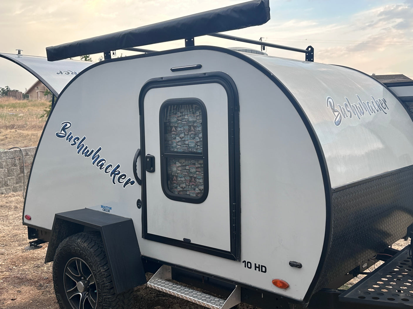 This Bushwhacker 10 HD teardrop RV rental, a compact white camper with off-road tires and roof awning, is ready for adventure.