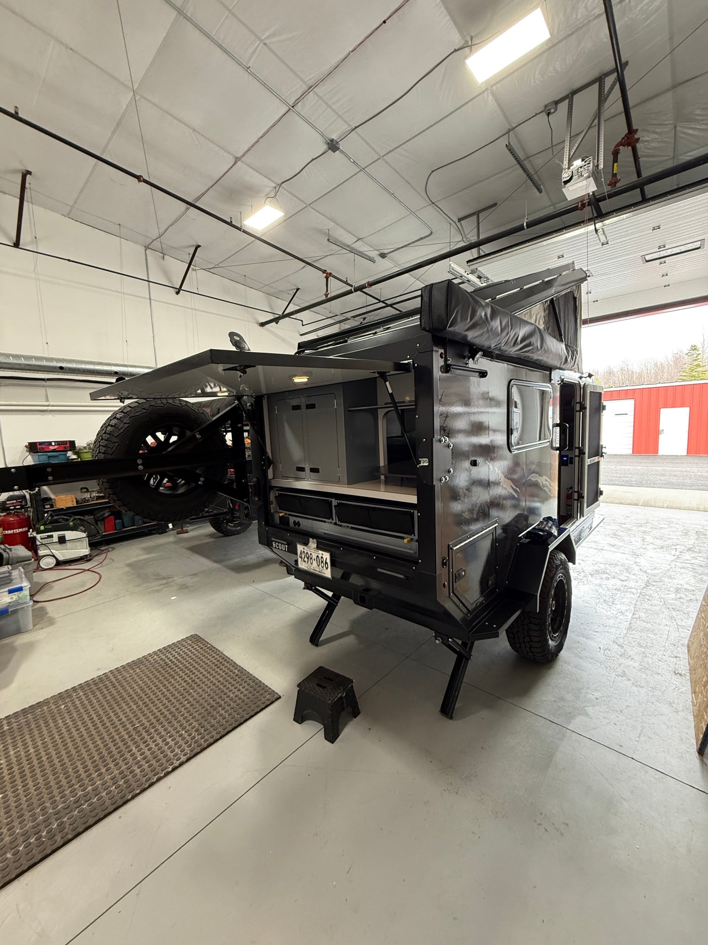 This rugged off-road camper trailer, perfect for rv rental adventures, is open in a workshop, showing its storage.