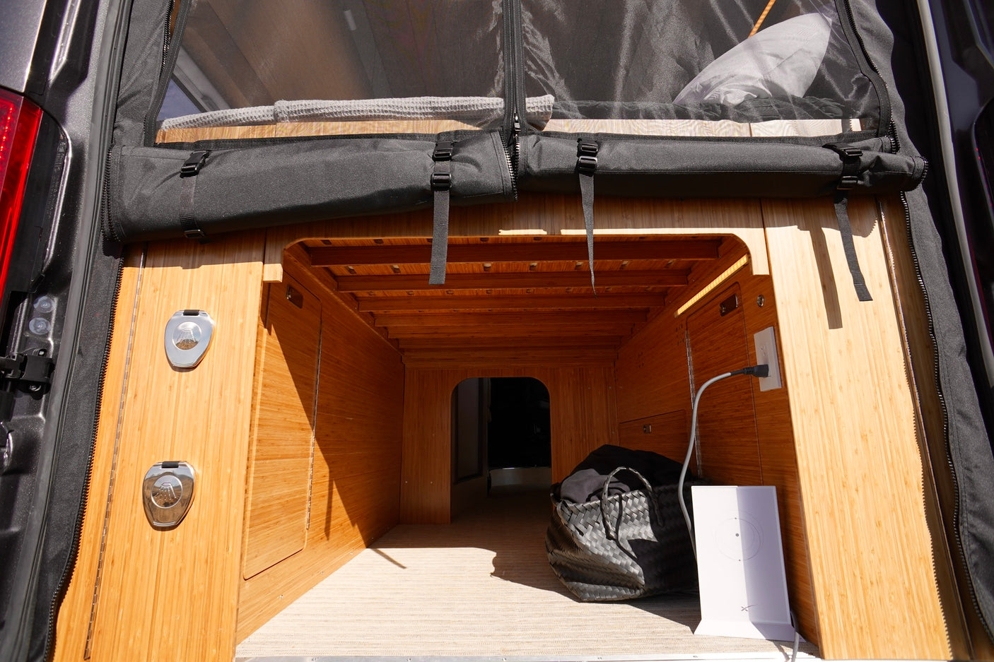 RV rental van's open rear storage area features bamboo paneling, a mesh screen, power outlet, and a Starlink device.