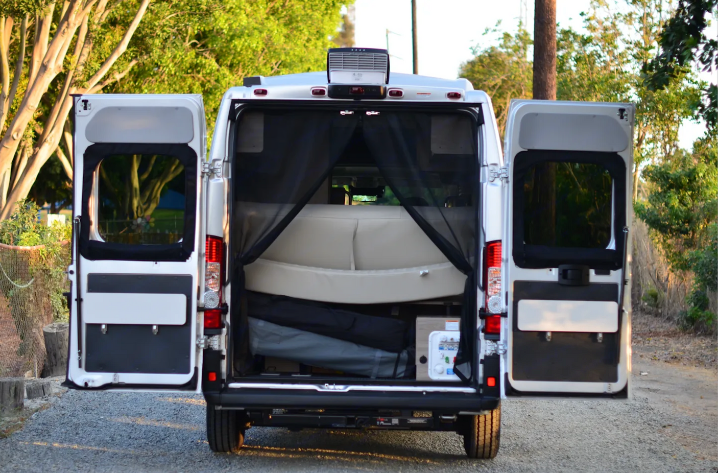 Open back doors of an RV rental revealing interior with a bed, storage, and black mesh screen.