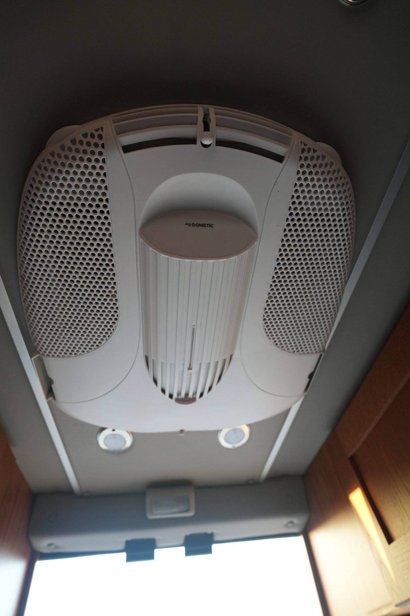 Overhead Dometic air conditioning unit in an rv rental, with perforated grilles, central vent, and ceiling lights.