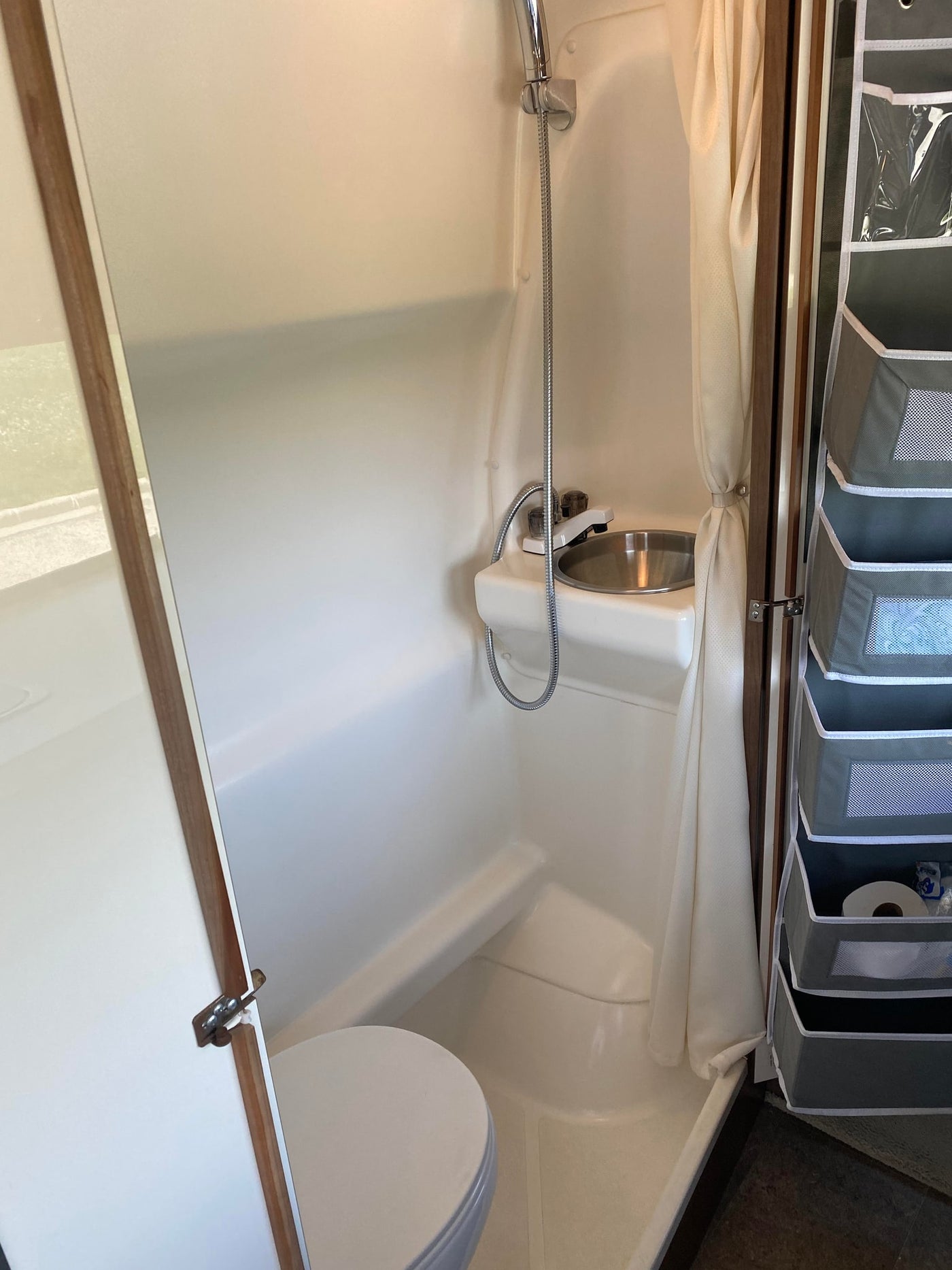An RV rental's compact wet bath showing a white toilet, small sink, shower, and hanging storage organizer. — photo 10