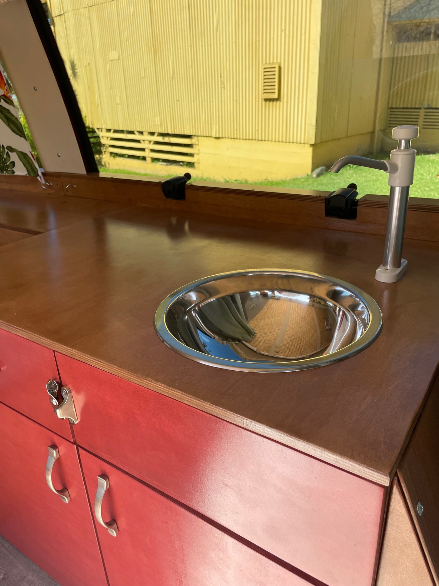 RV rental: A compact camper kitchen with a wooden counter, stainless steel sink, pump faucet, and red storage cabinets.