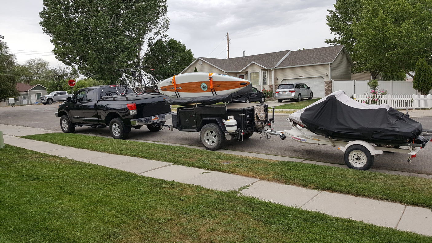 Outdoor enthusiast's dream: Black truck with bikes, an RV rental adventure trailer carrying a paddleboard, and a jet ski.