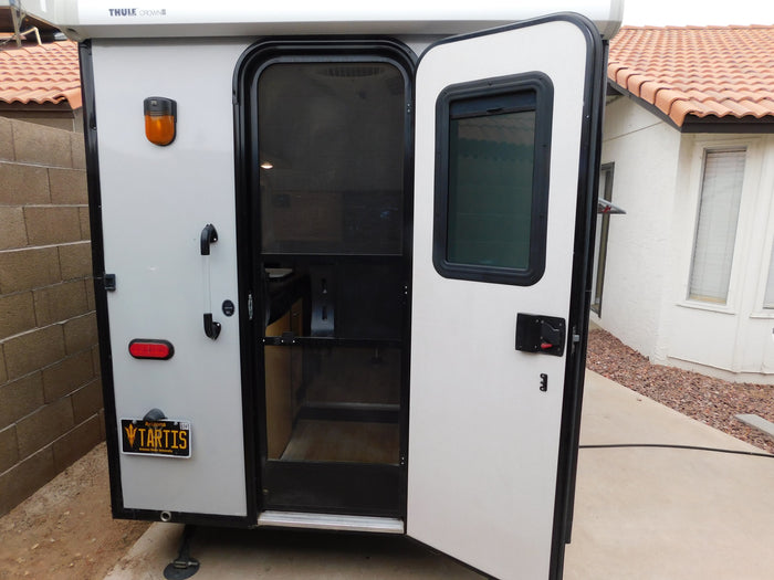 Light-colored compact RV rental with its rear door open, revealing the screen and interior. Arizona 'TARTIS' plate shown.