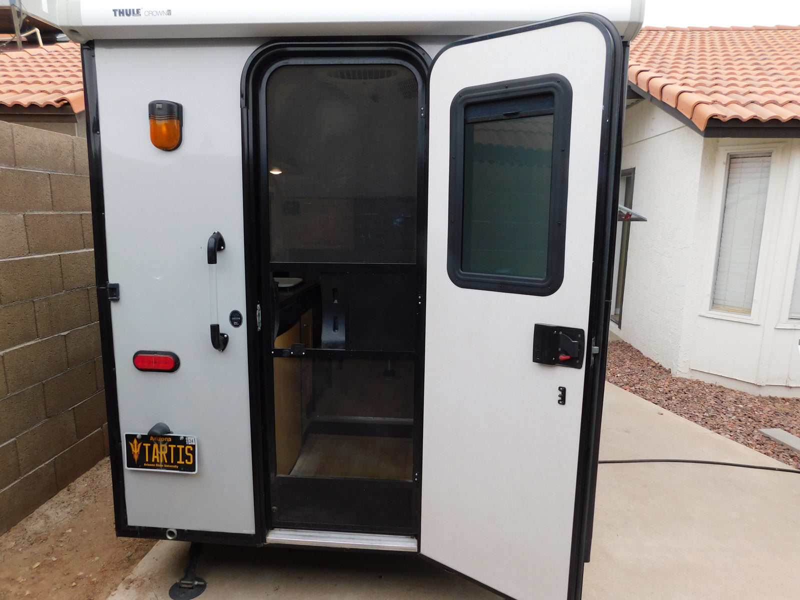 Light-colored compact RV rental with its rear door open, revealing the screen and interior. Arizona 'TARTIS' plate shown.
