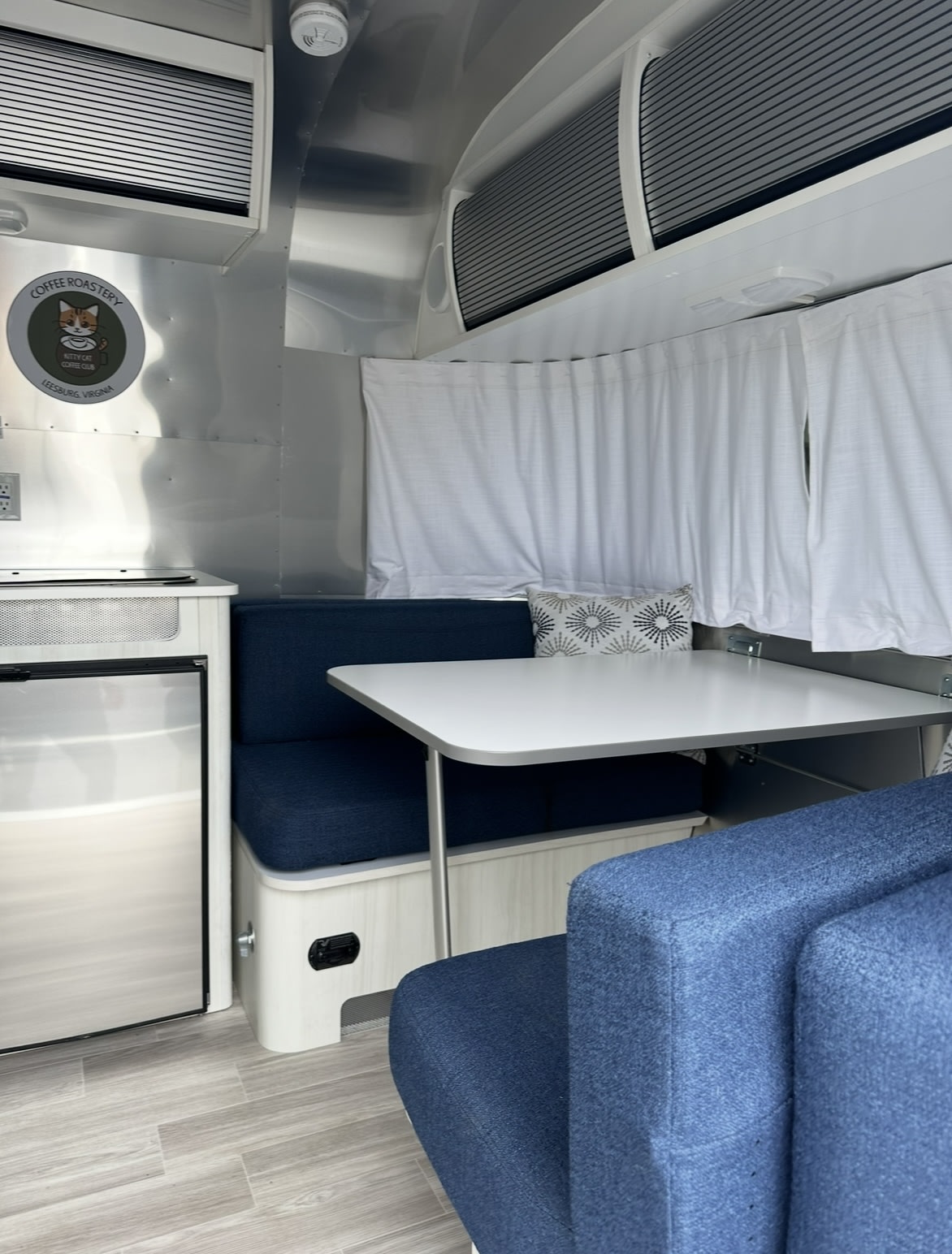 and privacy curtains.|An RV rental interior showing a dinette with blue benches