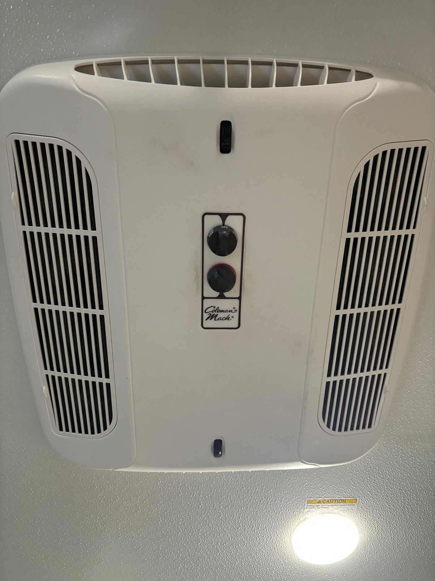 White Coleman Mach RV air conditioner on the ceiling of an rv rental, with manual fan and temp controls, and side vents.