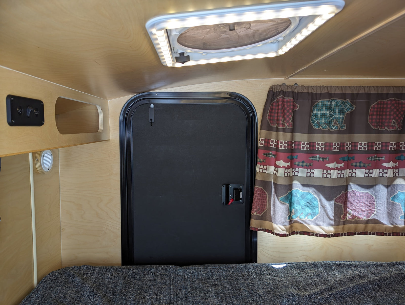 and campfire on a black background.|NOCO RV rental charging port showing a male electrical inlet with three pins.|View inside a compact RV rental: wood-paneled interior