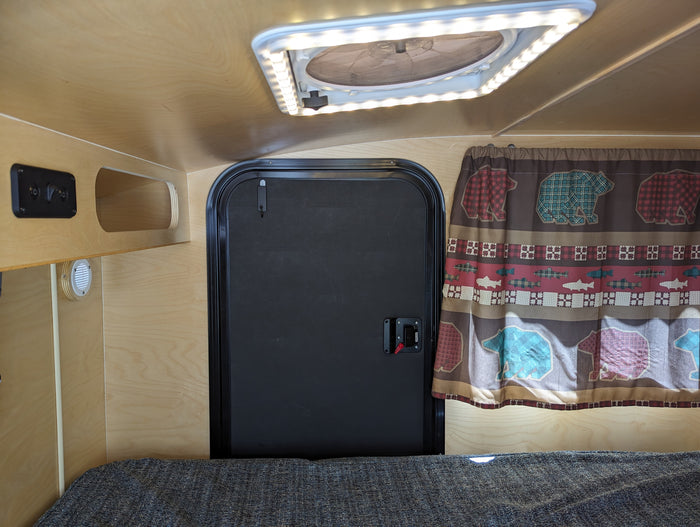 and campfire on a black background.|NOCO RV rental charging port showing a male electrical inlet with three pins.|View inside a compact RV rental: wood-paneled interior