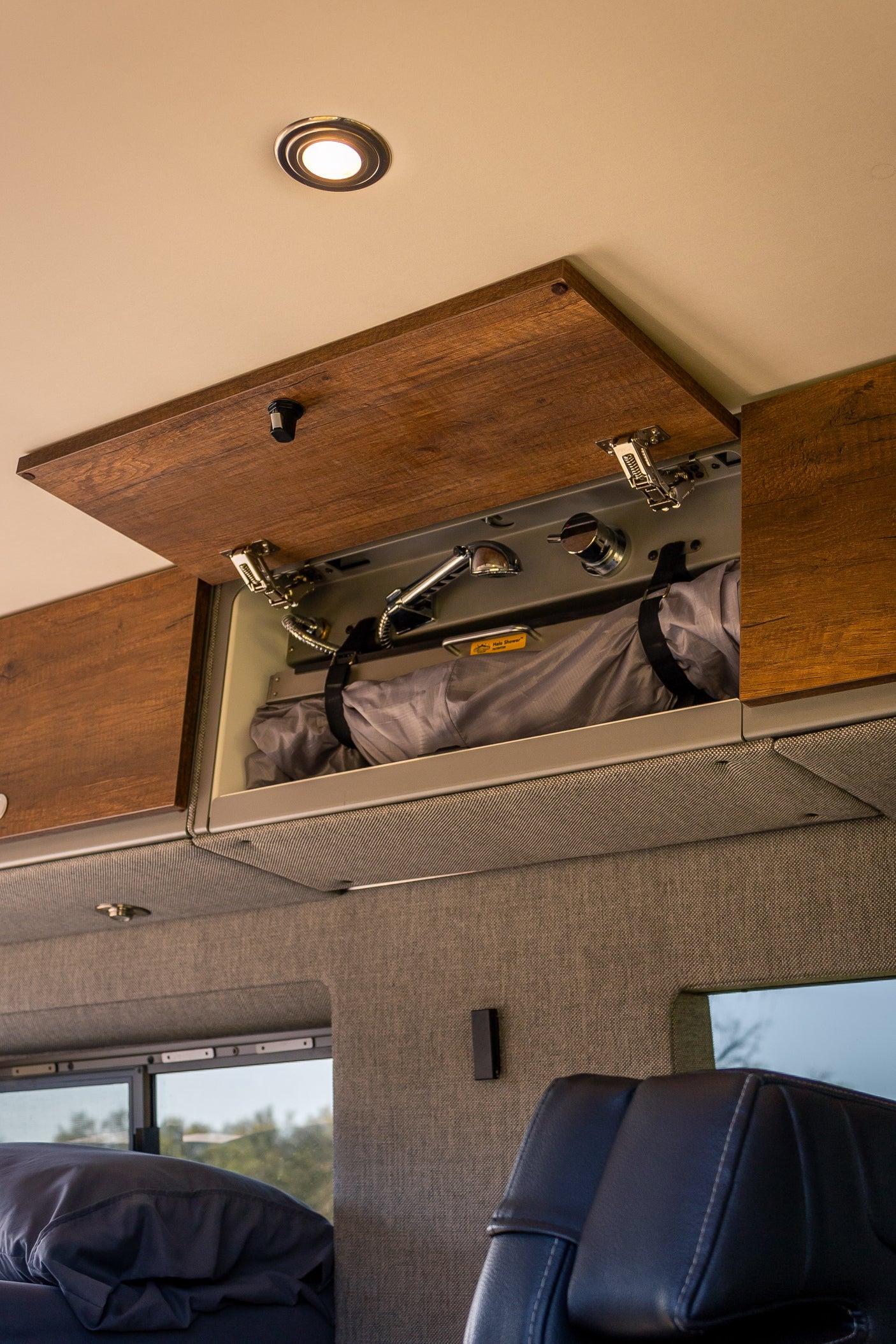 Explore this RV rental's interior: an open overhead cabinet reveals a portable shower system and stored gear, maximizing space.