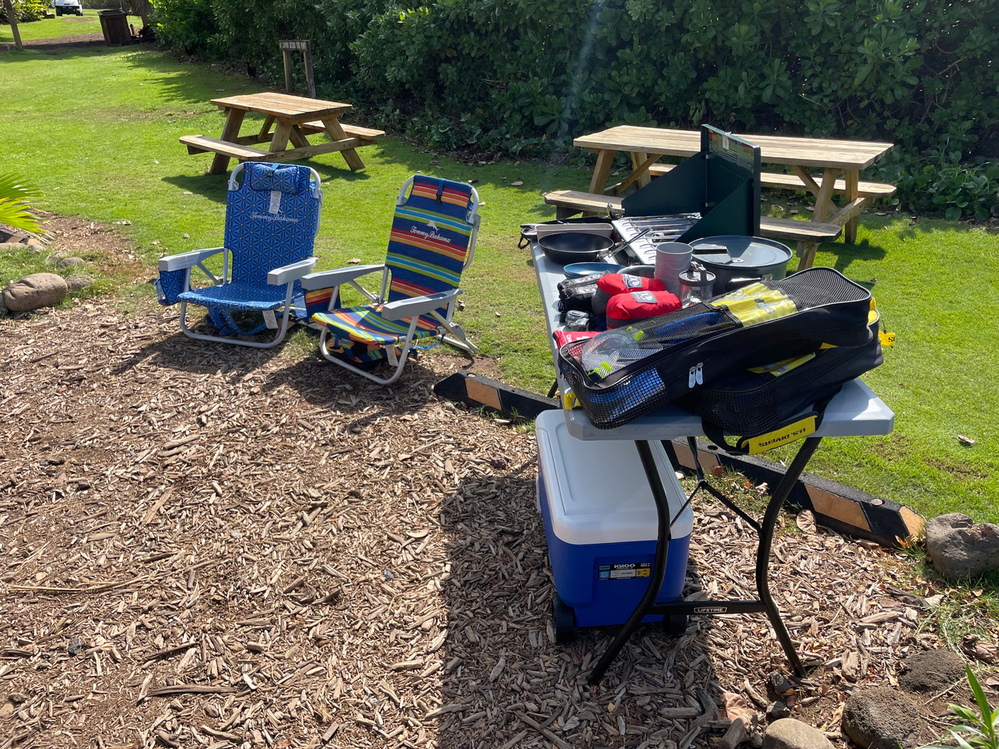 An RV rental provides this perfect outdoor setup: chairs, cooler, cooking gear, and a dive bag at a grassy campsite.