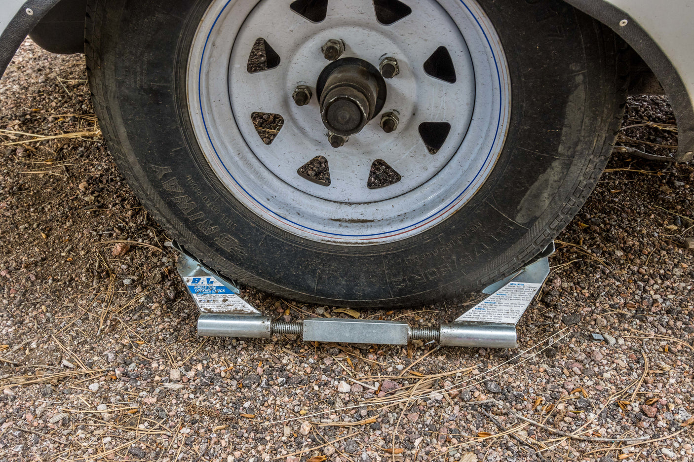 An RV rental tire is securely chocked on gravel with a BAL locking chock, ensuring stability and preventing movement.