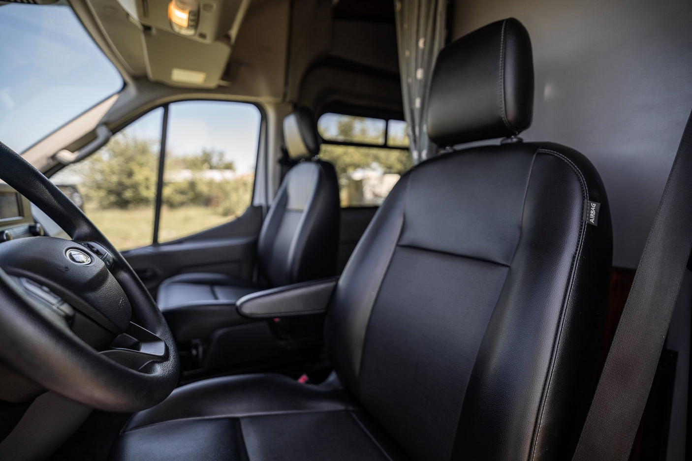 Explore this RV rental's inviting front cabin. View black leather seats & steering wheel, ready for your adventure.