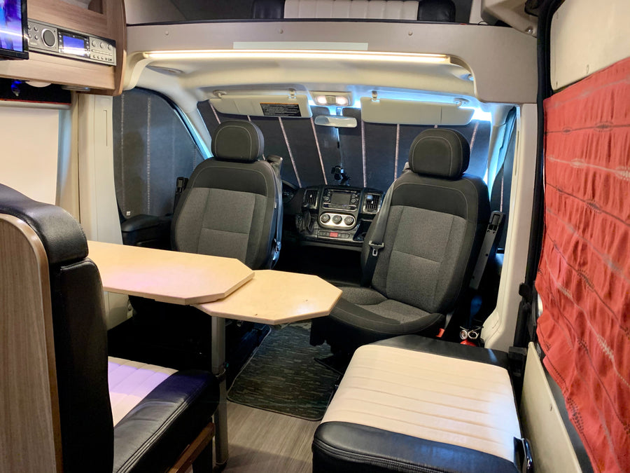 Interior of an RV rental camper van, showing swiveling front seats, a central table, and comfortable living area seating.