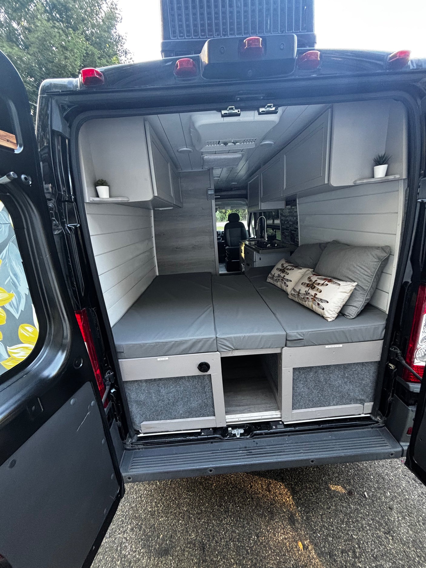 Interior of an RV rental camper van: a cozy bed, kitchen, and overhead storage for your travel needs.