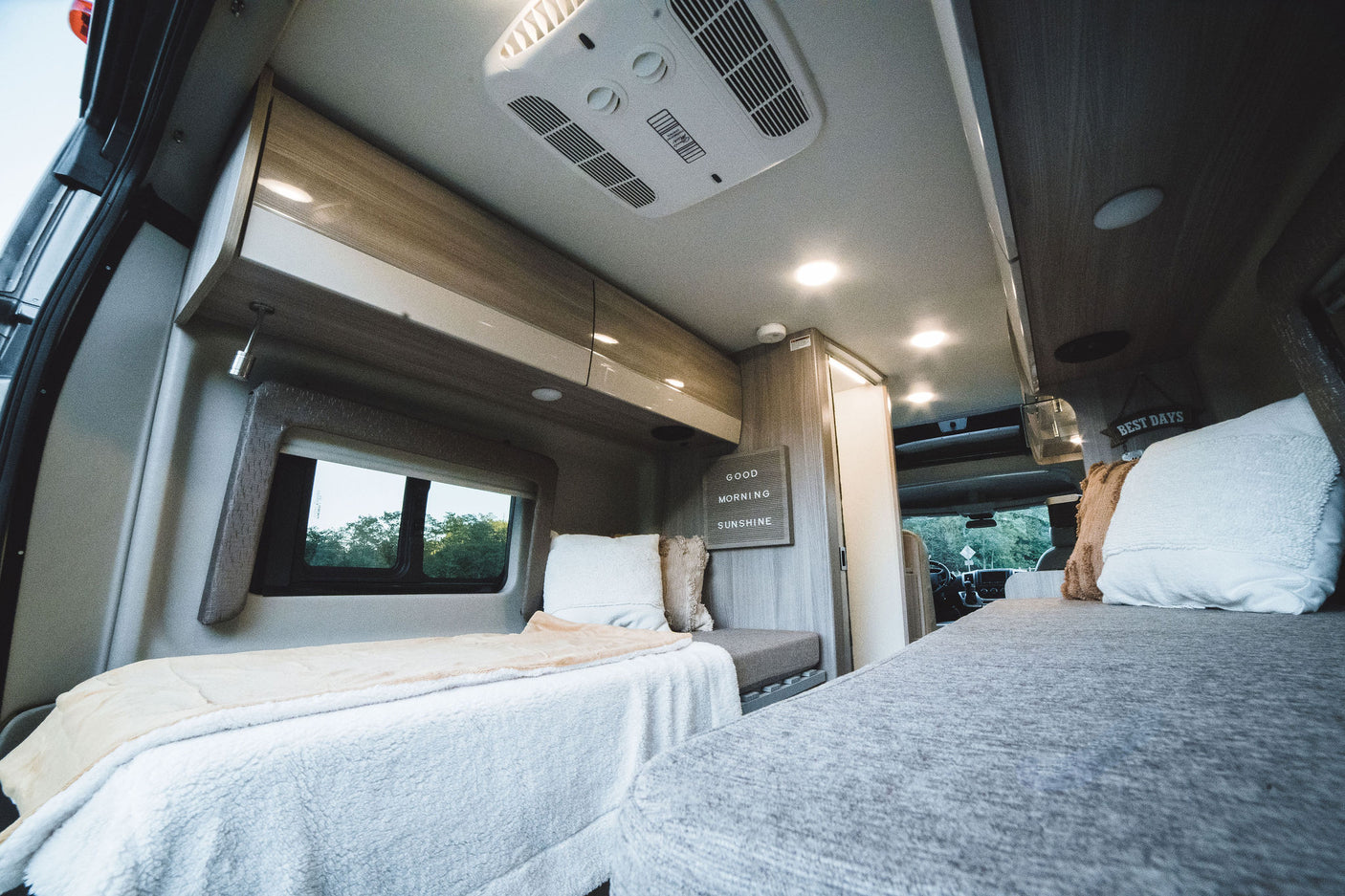 Spacious and modern RV rental interior, featuring comfortable beds, overhead storage, and AC. Enjoy cozy van life!