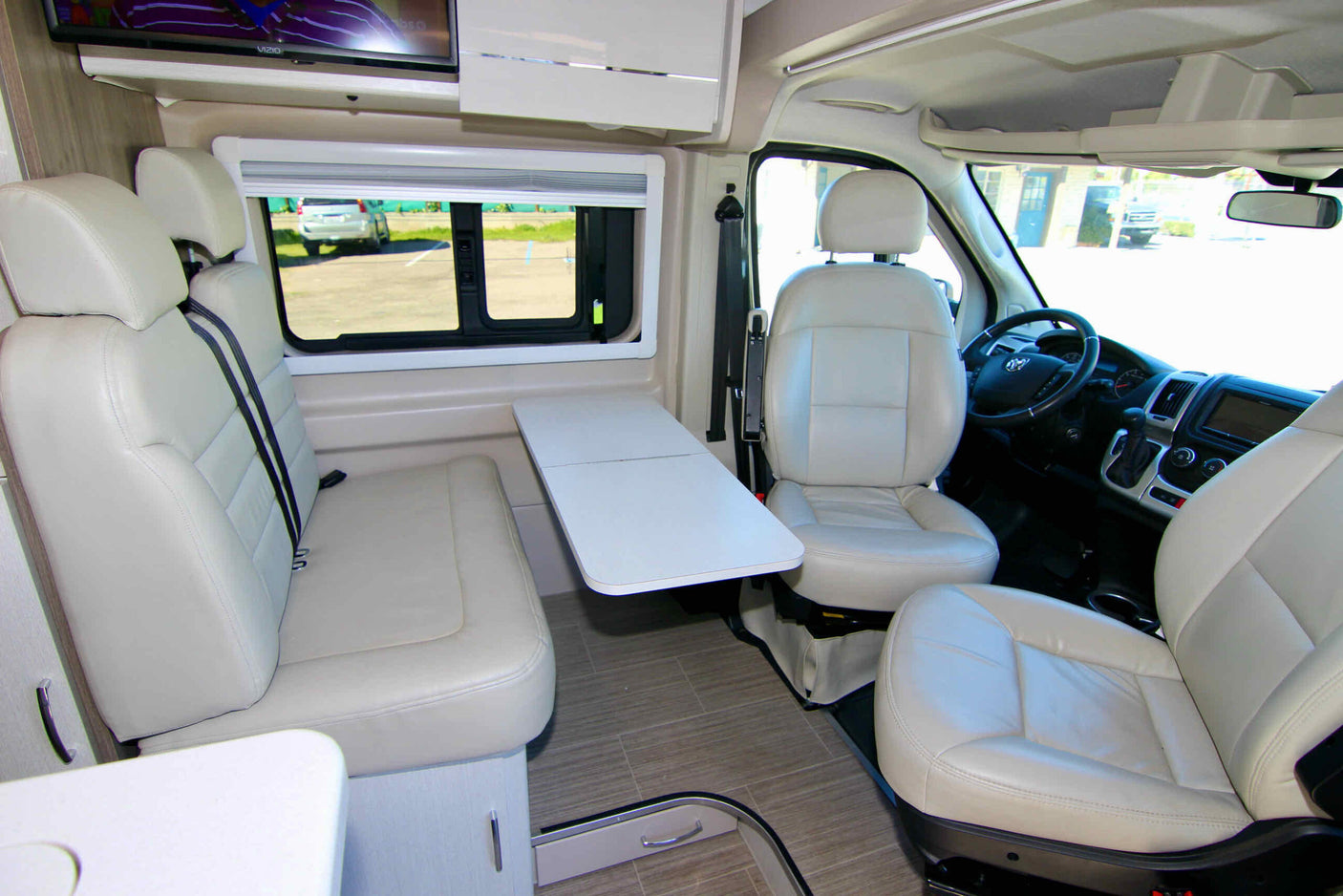 Bright and airy rv rental interior featuring cream leather seats, a movable table, and a TV for travel comfort.