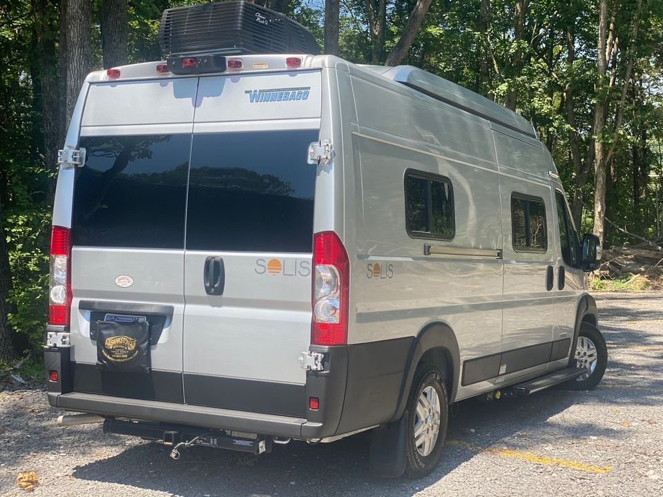 A silver Winnebago Solis camper van, excellent for an rv rental, parked in a wooded area.