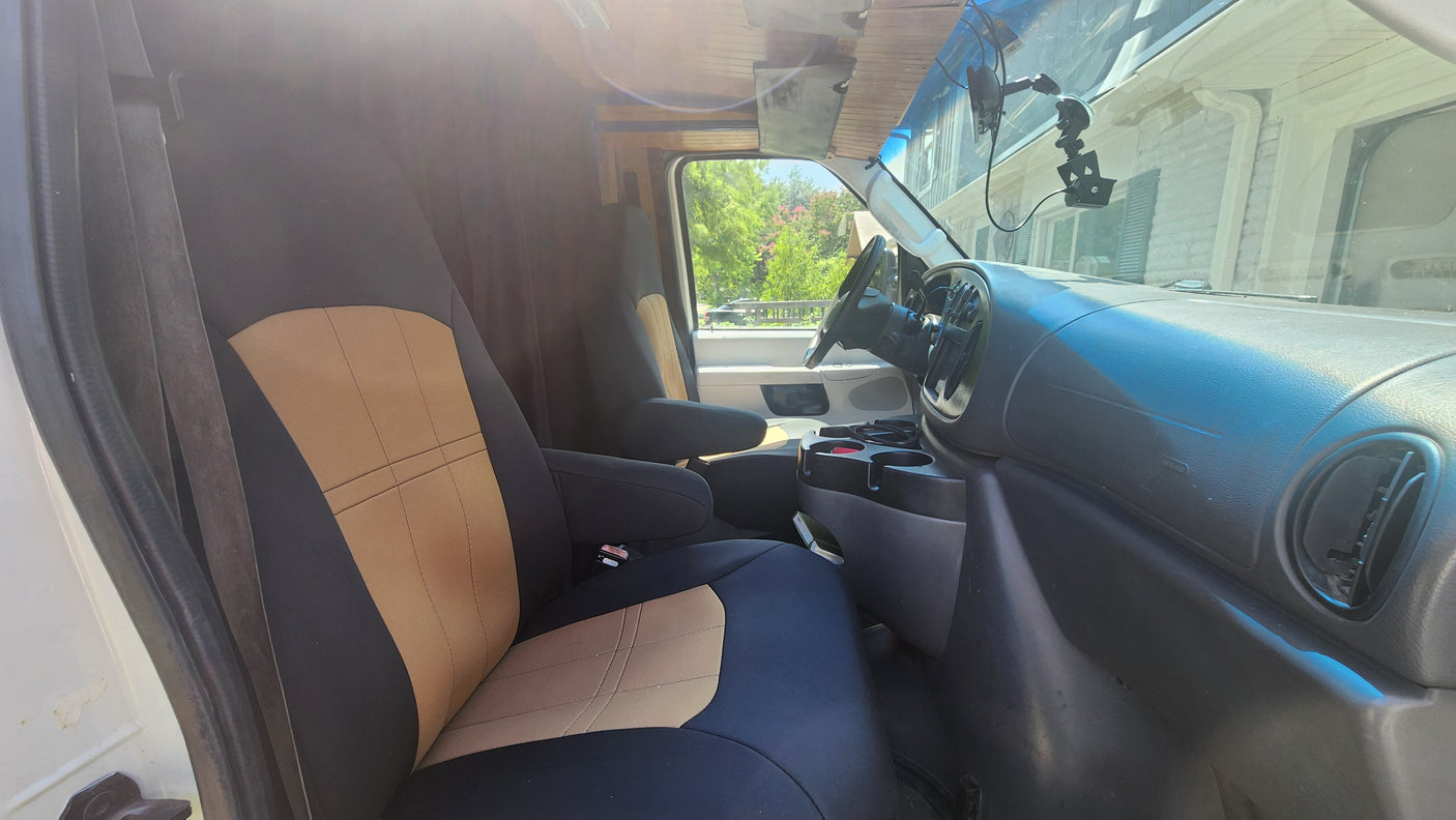 RV rental van's cozy interior: two-tone seats, dashboard, and steering wheel, with a bright outdoor view.