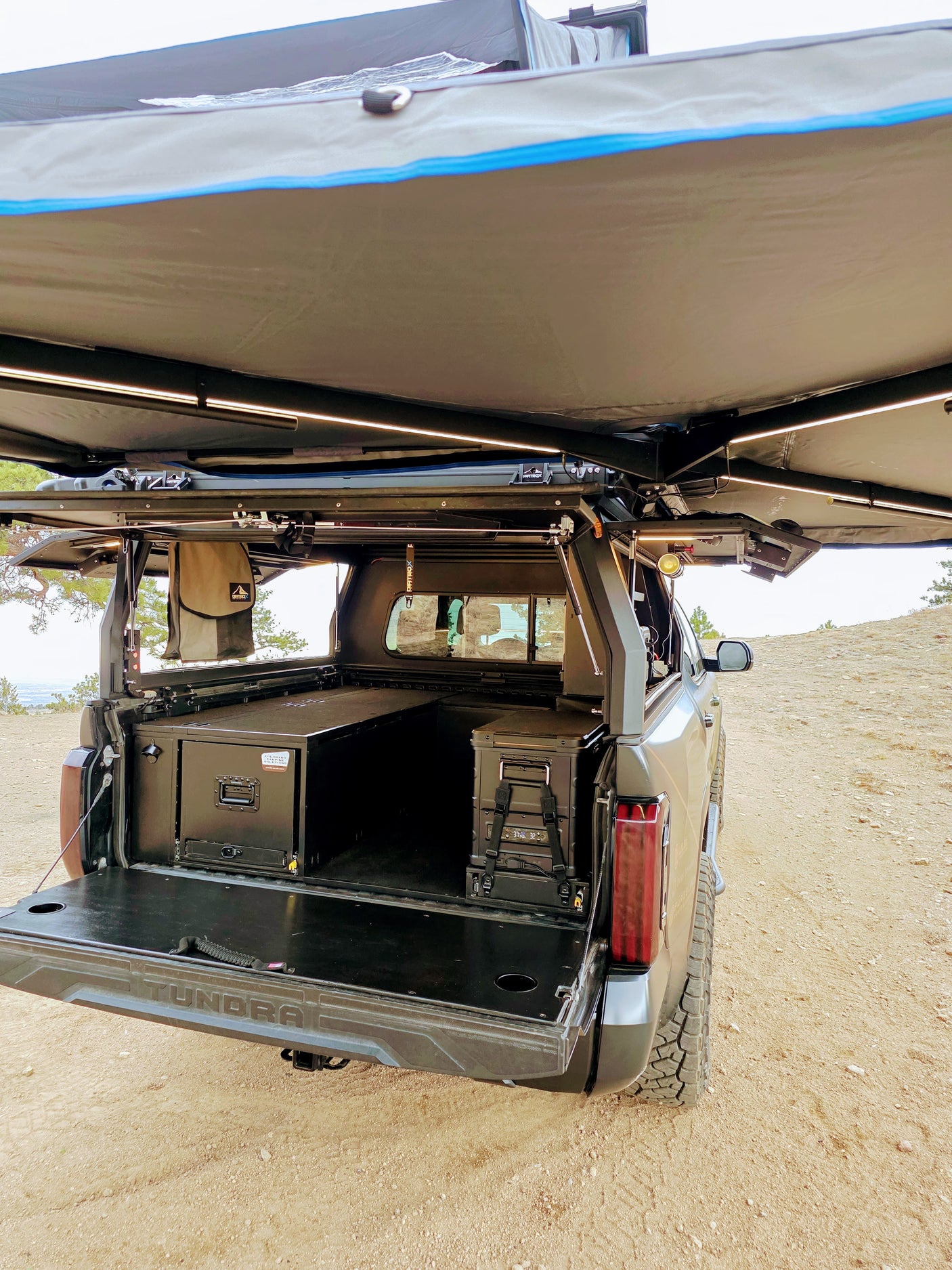 A Toyota Tundra pickup, perfect for an rv rental, highlights its custom overland camping setup with storage, fridge, and awning.