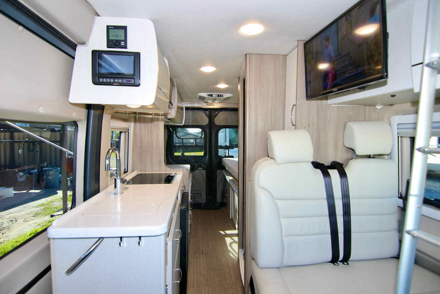 View inside a sleek rv rental: a compact kitchen, electronic controls, comfortable seating, and wall-mounted TV.