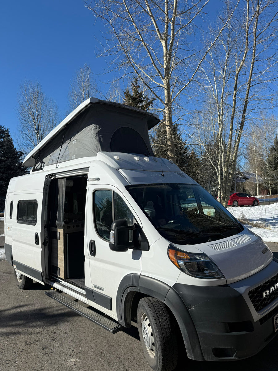 White pop-top camper van with open side door, ready for your rv rental. Sunny winter day, bare trees in background.