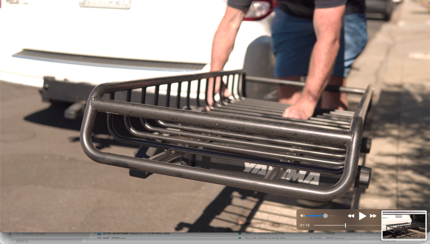 A person attaches a black Yakima cargo carrier to a white RV rental vehicle, ready for adventure.
