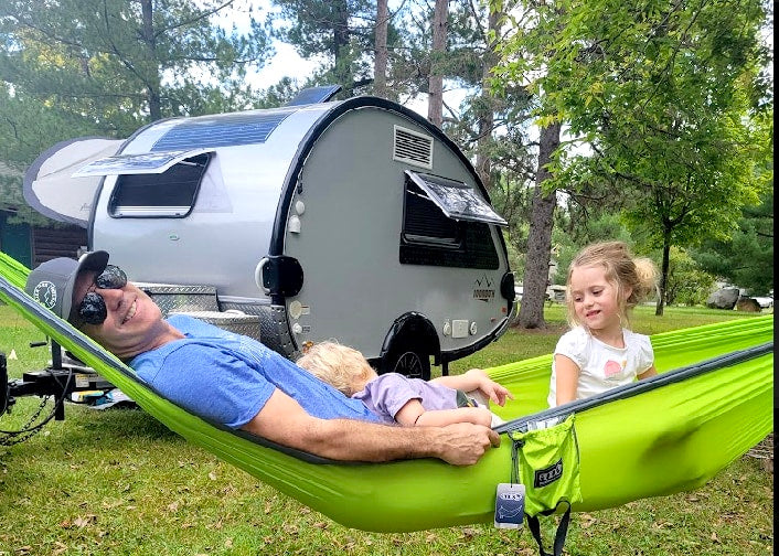 Dad and kids relax in a vibrant green hammock, enjoying outdoor family fun beside their rv rental.