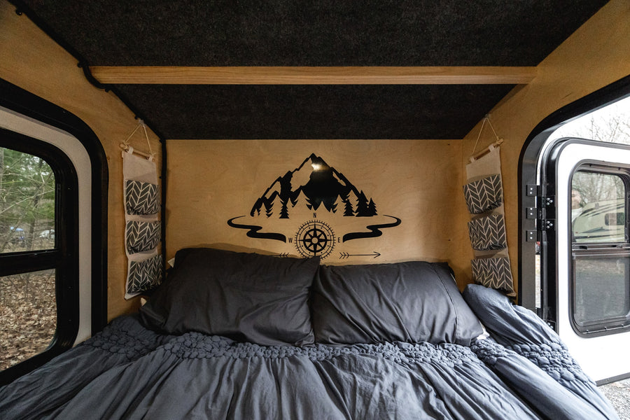 Relax in this cozy RV rental's interior. Features a comfortable bed, wood accents, and adventure-themed wall art.