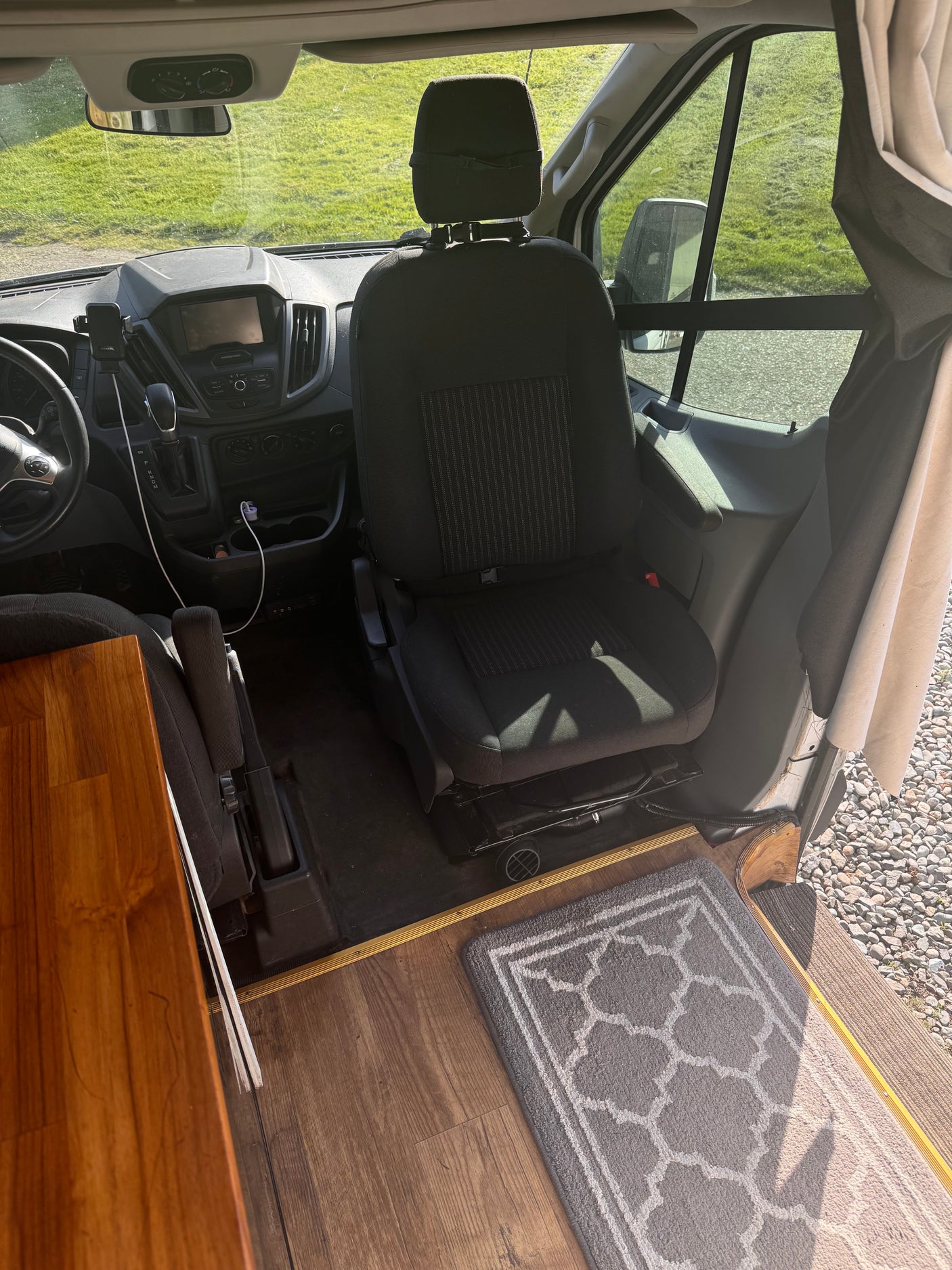 Inside an RV rental, the front cab features a dashboard, driver's area, and a swiveling passenger seat with wood flooring.