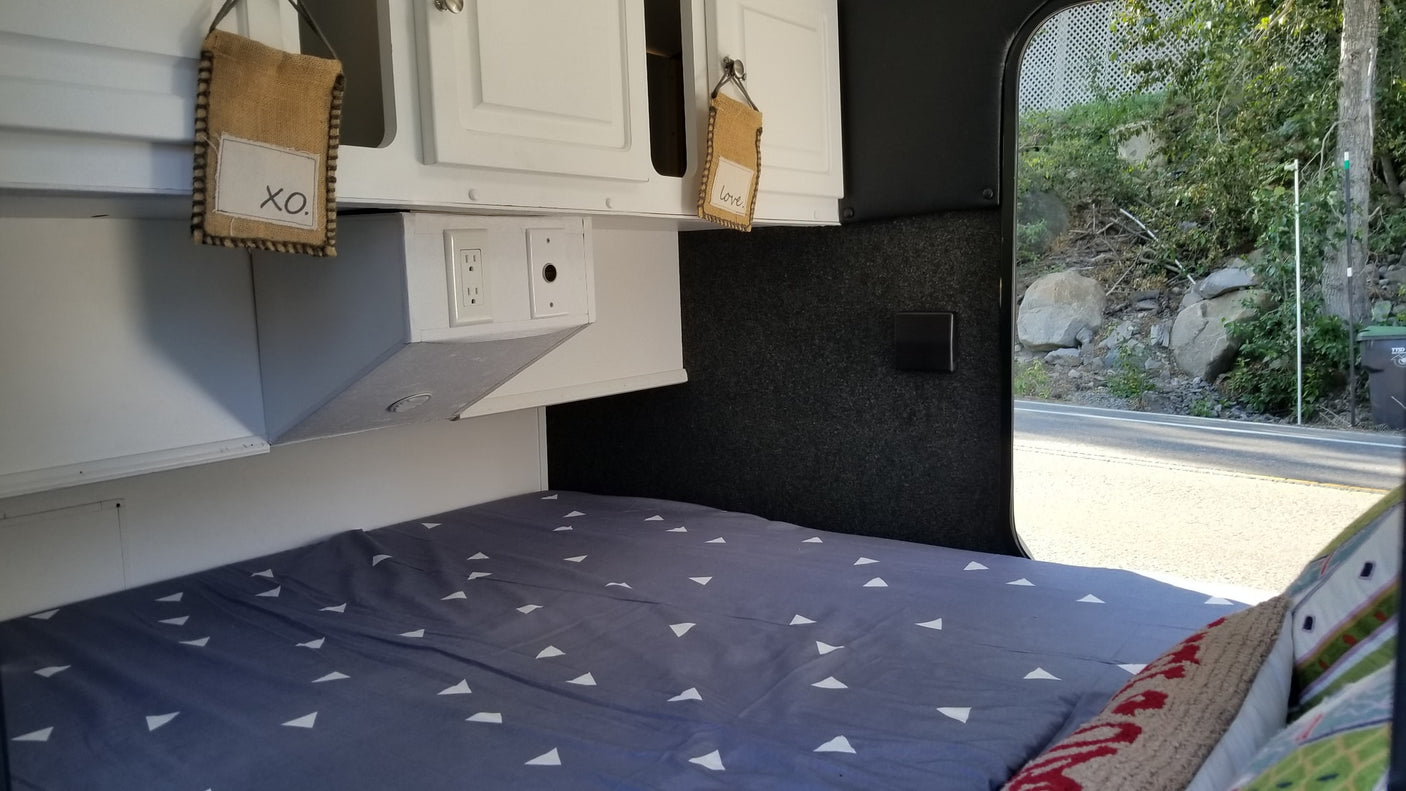 Compact RV rental cabin interior featuring a comfy bed, overhead cabinets, and essential outlets.