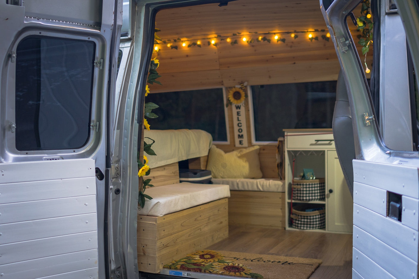 Step inside this cozy RV rental! Wood-paneled van interior with warm lights, comfy seating, and sunflower welcome decor.