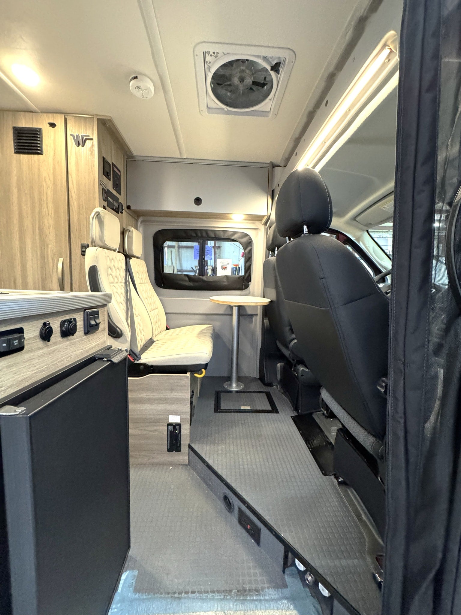 This RV rental interior shows swiveling front seats, a dining table, kitchenette, and overhead storage, perfect for a road trip.