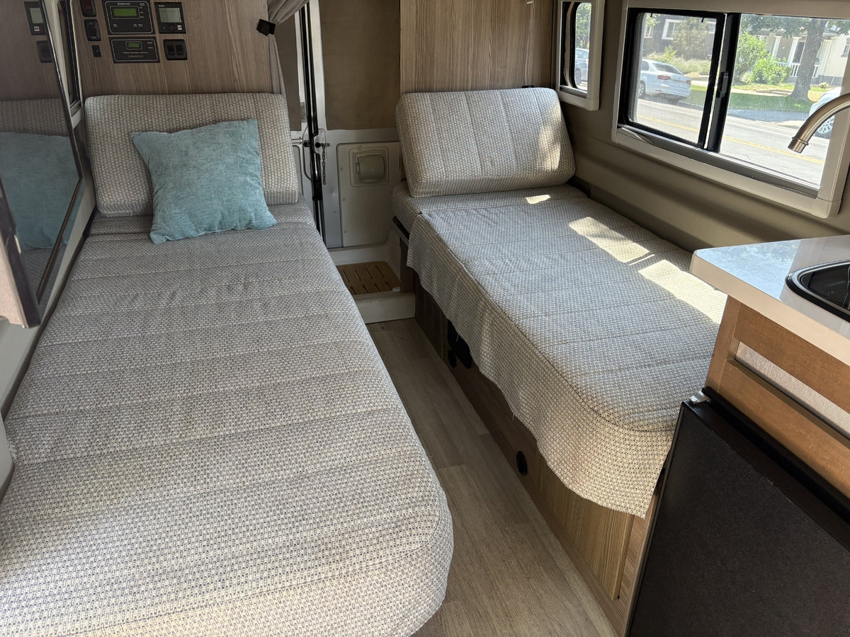 Inside an RV rental: two single beds with light fabric covers, wall controls, and a window showing street views. — photo 7