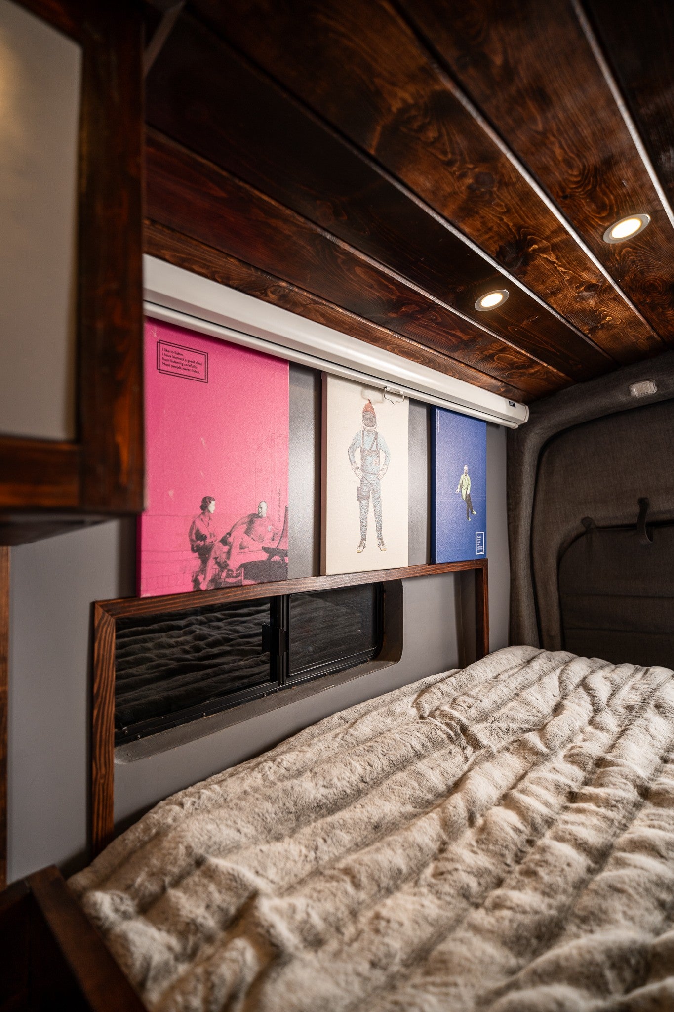 Cozy van life RV rental interior: plush bed, dark wood ceiling, and artistic sliding panels covering the window.