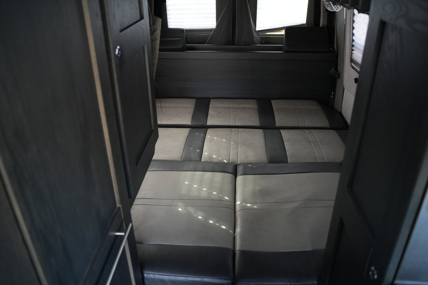 RV rental: Interior with open dark wood doors framing a convertible gray & dark cushion seating/bed & back window.