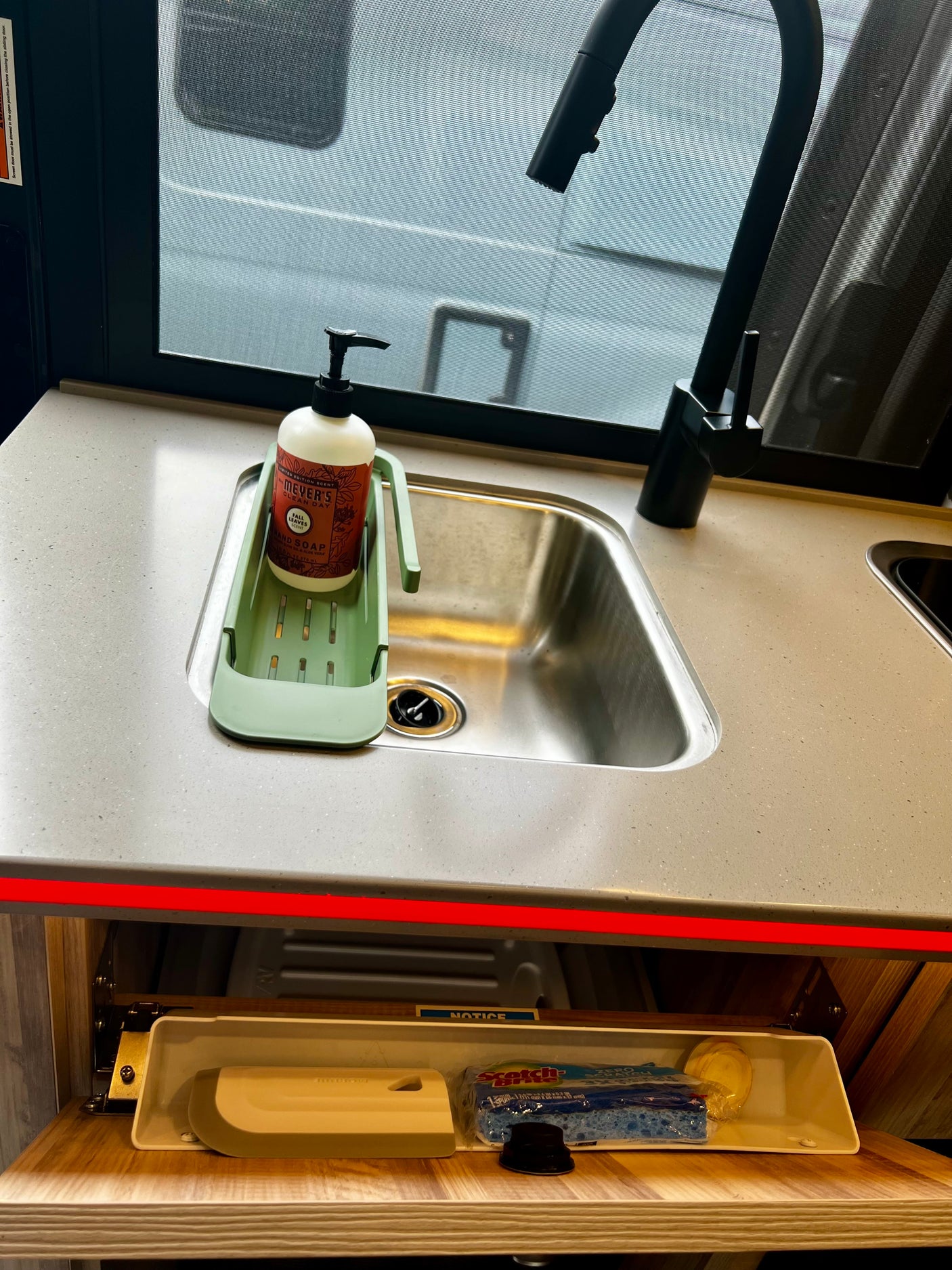 **RV rental** kitchen sink area with hand soap, black faucet, and neatly stored cleaning supplies in a pull-out tray.