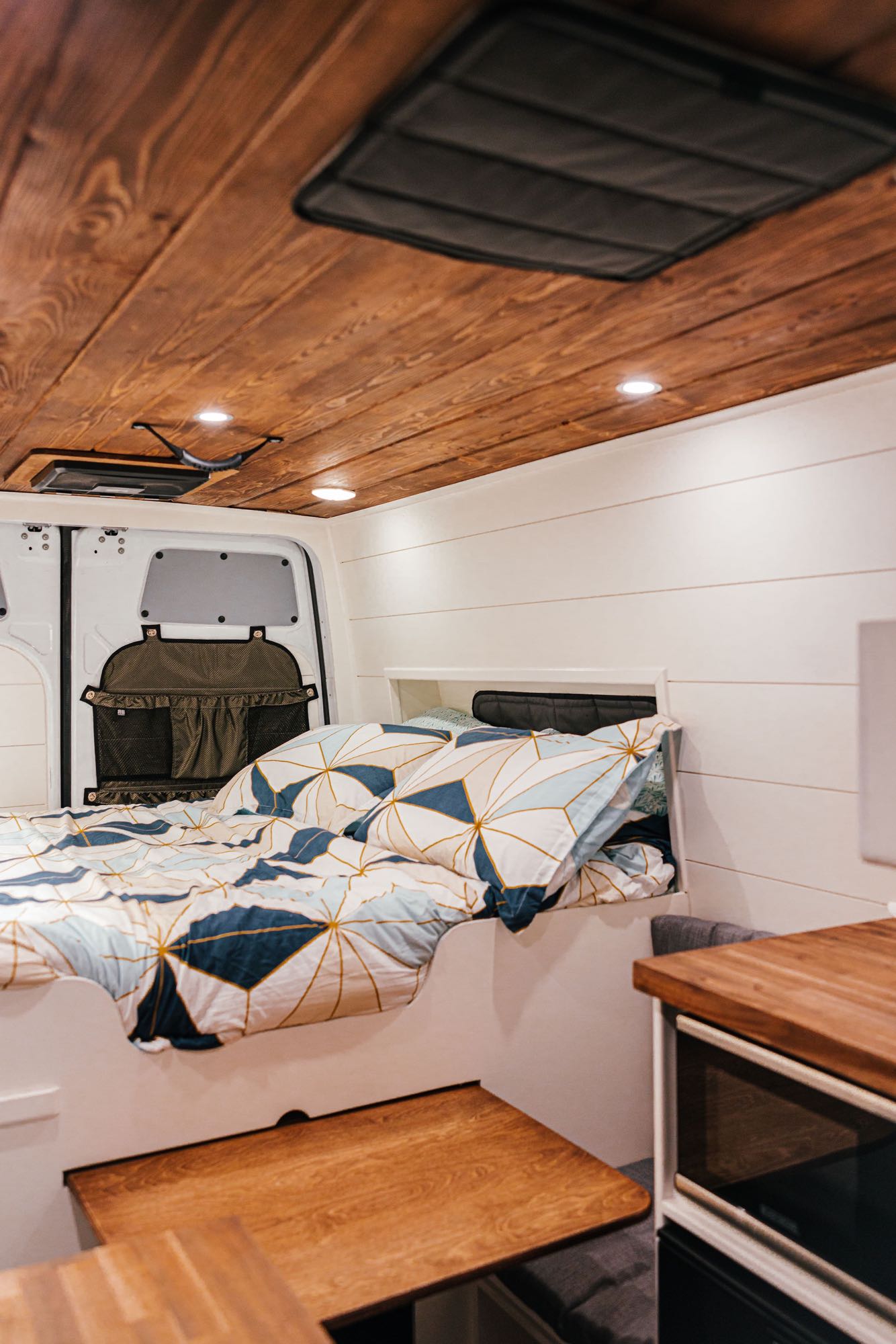 Explore this RV rental's cozy interior: bed with patterned bedding, wood ceiling, white walls, and built-in kitchen.