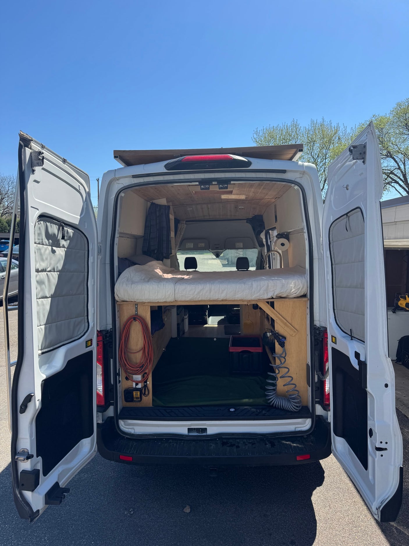 RV rental camper van with open back doors, showcasing a custom interior, elevated bed, storage, and utilities.