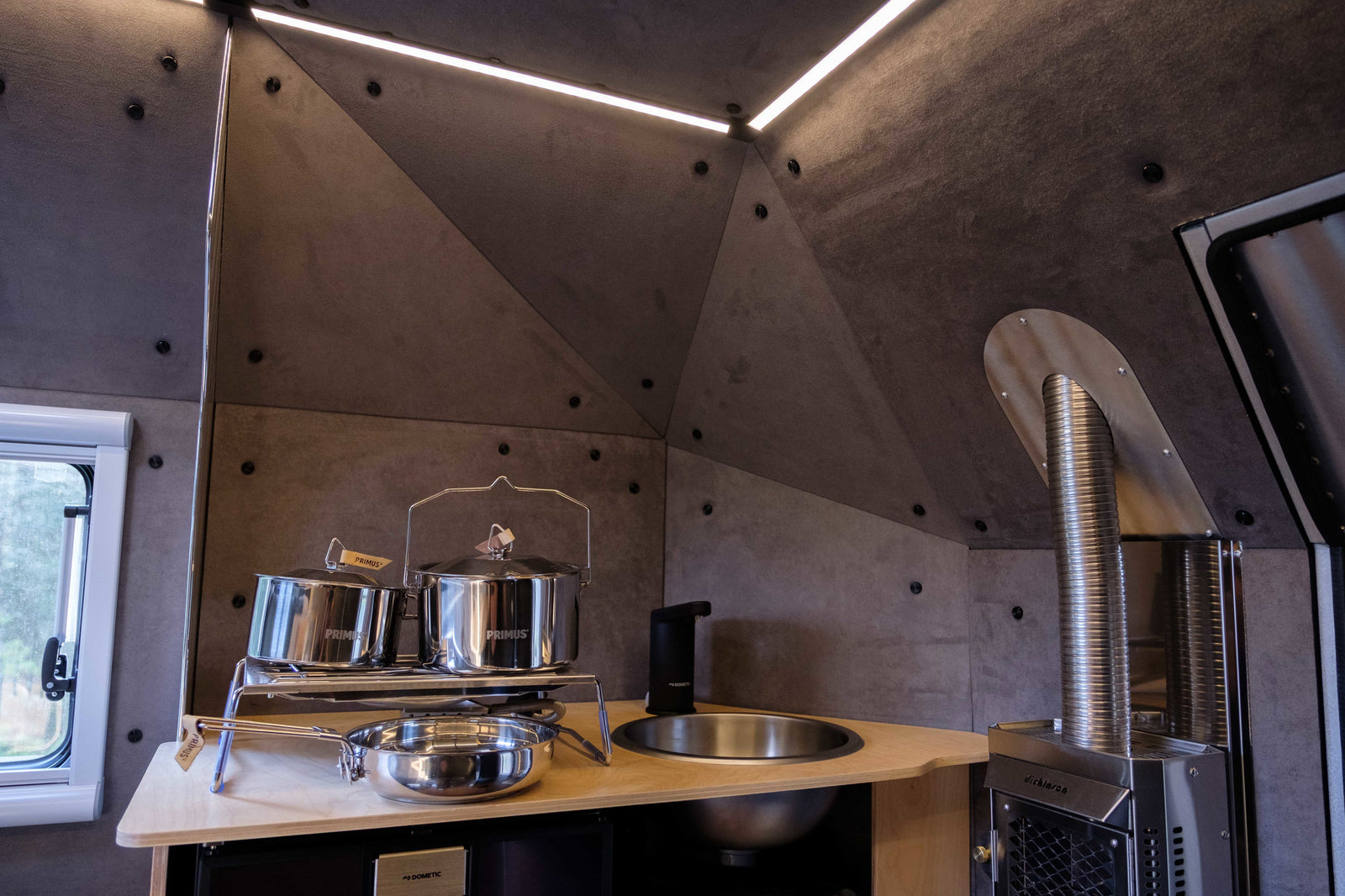 Modern RV rental kitchen with Primus pots, Dometic sink, Dickinson stove. Compact & complete.